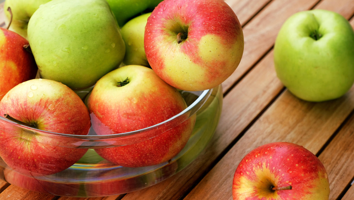 Bowl of red and green apples in a glass bowl on a wooden surface