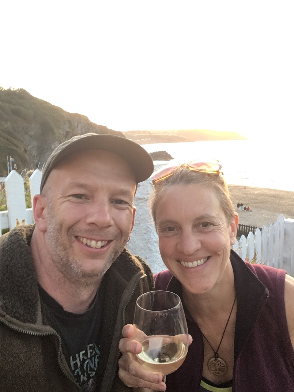Two people smiling outdoors with one holding a glass.